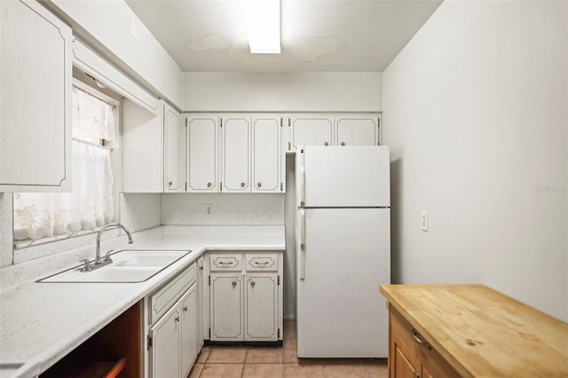 kitchen featuring freestanding refrigerator, a sink, light tile patterned flooring, and butcher block counters
