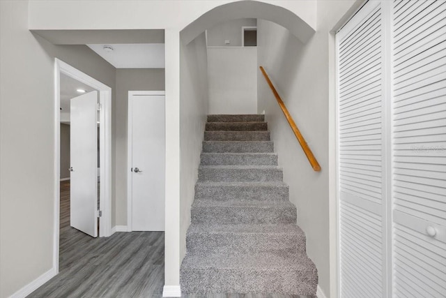 staircase featuring wood finished floors, baseboards, and arched walkways