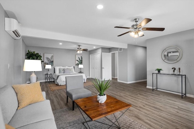 living area featuring a wall mounted air conditioner, ceiling fan, wood finished floors, baseboards, and recessed lighting