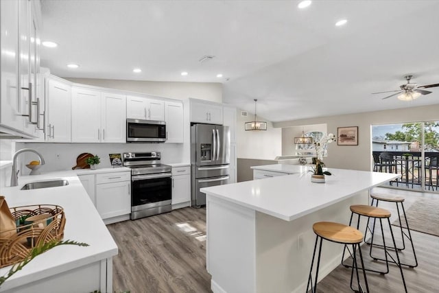 kitchen with appliances with stainless steel finishes, a sink, a kitchen island, lofted ceiling, and light wood-style floors