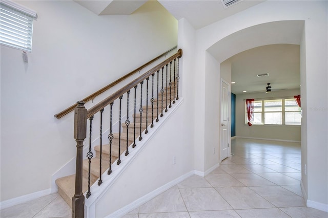 stairway with arched walkways, ceiling fan, tile patterned floors, and baseboards