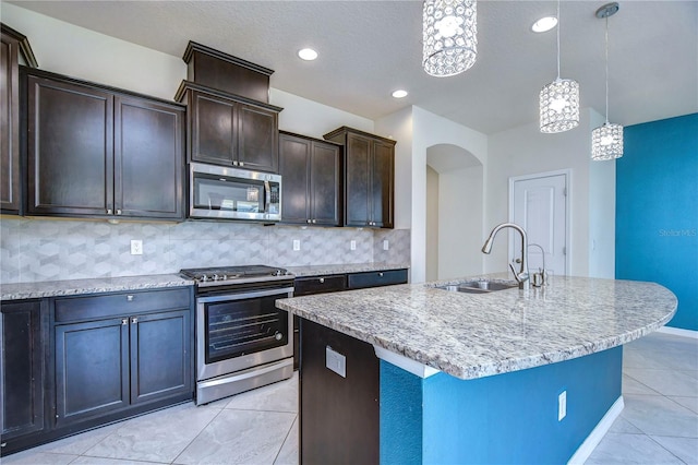 kitchen featuring appliances with stainless steel finishes, a sink, light tile patterned flooring, light stone counters, and arched walkways