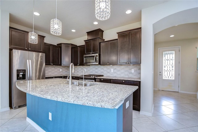 kitchen featuring stainless steel appliances, arched walkways, a sink, light tile patterned floors, and dark brown cabinetry