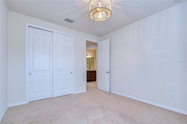 unfurnished bedroom with carpet, a chandelier, baseboards, and a closet