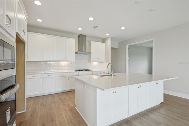 kitchen featuring a sink, wall chimney exhaust hood, light wood-style floors, light countertops, and recessed lighting