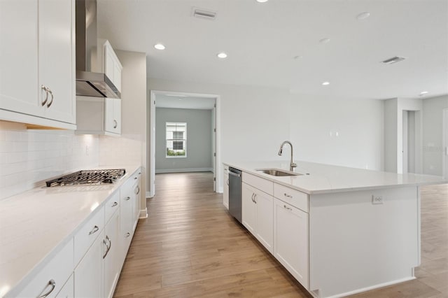 kitchen with wall chimney range hood, a sink, stainless steel appliances, backsplash, and light wood-type flooring