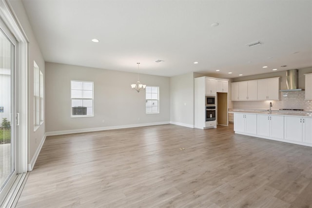 kitchen with stainless steel appliances, wall chimney range hood, a chandelier, open floor plan, and plenty of natural light