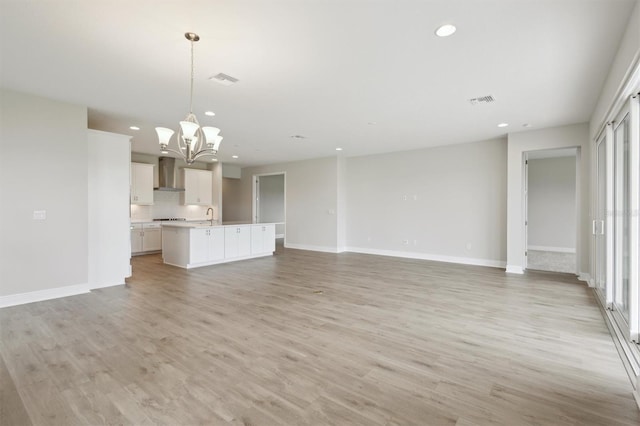 unfurnished living room featuring a chandelier, recessed lighting, light wood-type flooring, baseboards, and a sink