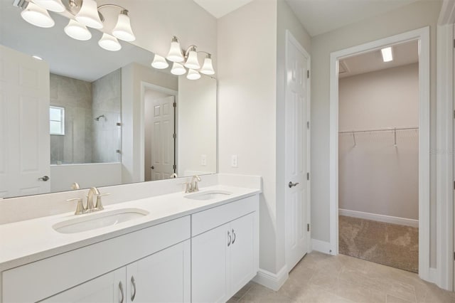 full bathroom with a tile shower, double vanity, a spacious closet, baseboards, and tile patterned floors