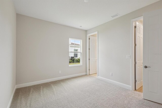 spare room featuring light colored carpet and baseboards