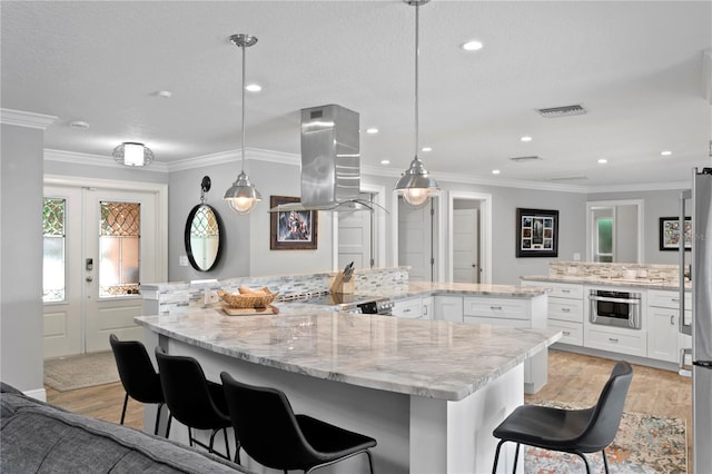 1960 Montana Ave NE, Saint Petersburg, FL 33703 - kitchen featuring island exhaust hood, light wood finished floors, a large island with sink, stainless steel oven, and white cabinetry