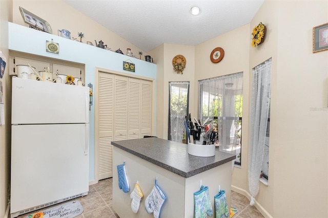 640 Lake Dexter Cir, Winter Haven, FL 33884 - kitchen featuring freestanding refrigerator, dark countertops, light tile patterned floors, a center island, and a textured ceiling
