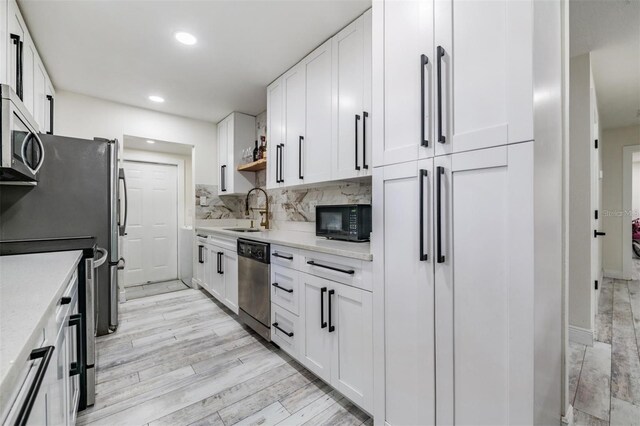 kitchen featuring a sink, appliances with stainless steel finishes, light wood finished floors, white cabinets, and tasteful backsplash