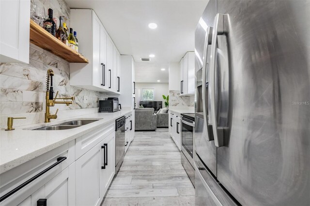 kitchen with appliances with stainless steel finishes, a sink, open shelves, tasteful backsplash, and light stone counters