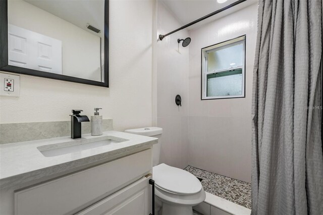 bathroom with toilet, tiled shower, and vanity