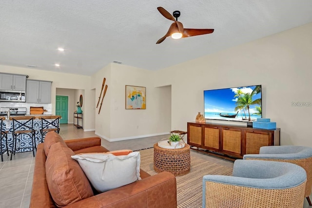 living area featuring a ceiling fan, light tile patterned floors, baseboards, and a textured ceiling