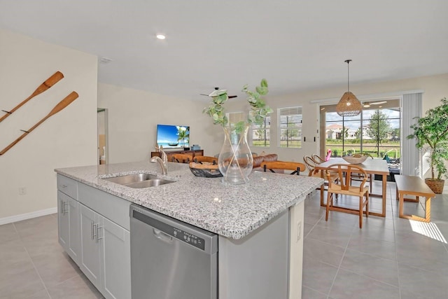 kitchen with stainless steel dishwasher, a sink, light tile patterned flooring, a kitchen island with sink, and light stone counters