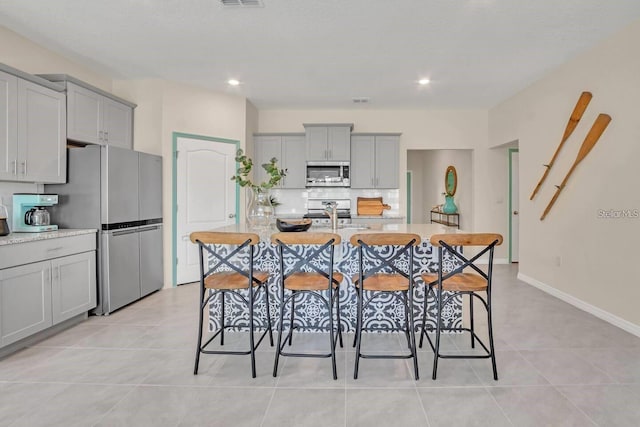 kitchen with appliances with stainless steel finishes, gray cabinetry, light tile patterned floors, recessed lighting, and decorative backsplash