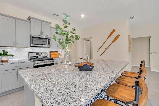 kitchen with stainless steel appliances, a sink, tasteful backsplash, an island with sink, and a kitchen bar
