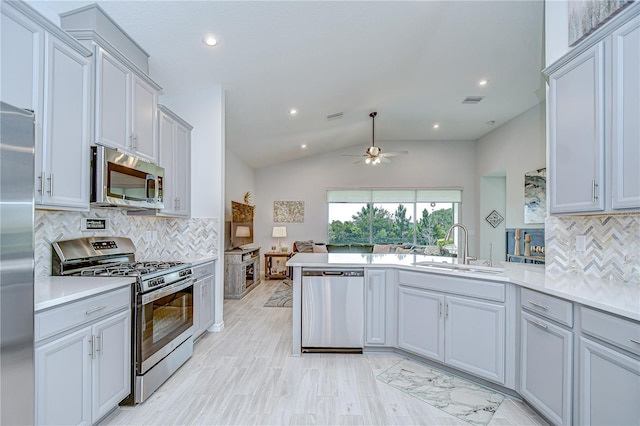 kitchen featuring appliances with stainless steel finishes, a sink, a ceiling fan, a peninsula, and backsplash