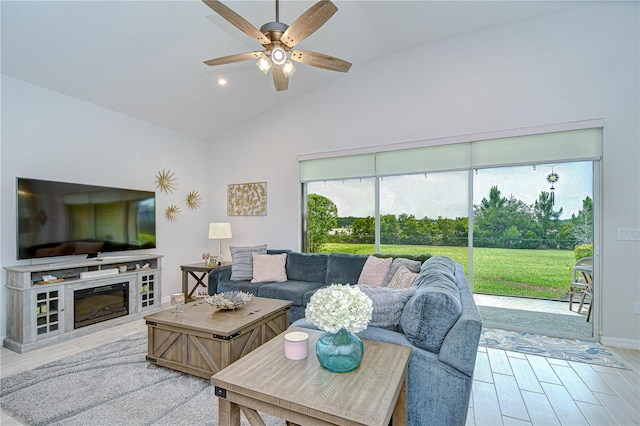 living area featuring ceiling fan, wood finished floors, high vaulted ceiling, and a glass covered fireplace