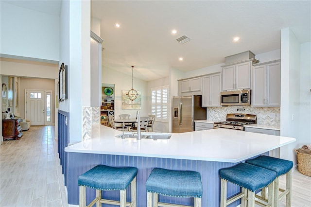 kitchen with stainless steel appliances, a sink, a kitchen bar, decorative backsplash, and lofted ceiling
