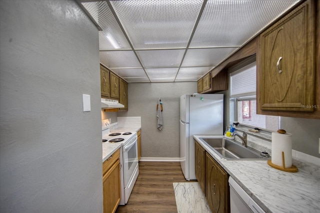 kitchen featuring white appliances, under cabinet range hood, a sink, baseboards, and dark wood-style flooring