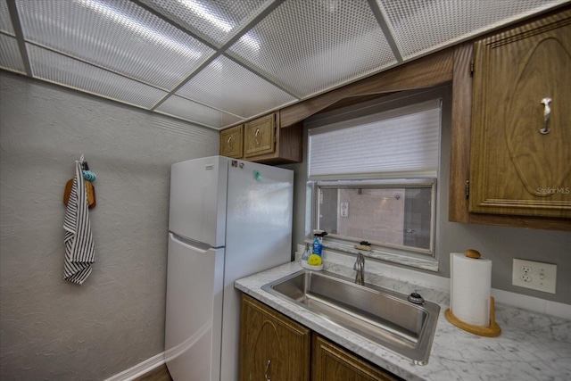kitchen featuring freestanding refrigerator, light countertops, a sink, and brown cabinets