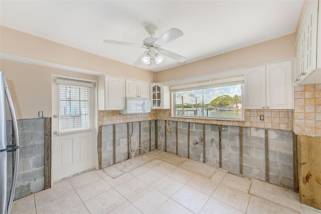 365 La Hacienda Dr, Indian Rocks Beach, FL 33785 - kitchen with white microwave, freestanding refrigerator, glass insert cabinets, light tile patterned floors, and plenty of natural light