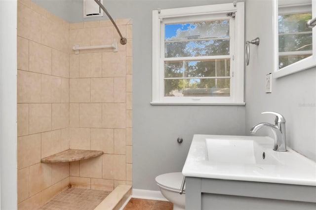 full bathroom with a tile shower, toilet, vanity, and baseboards