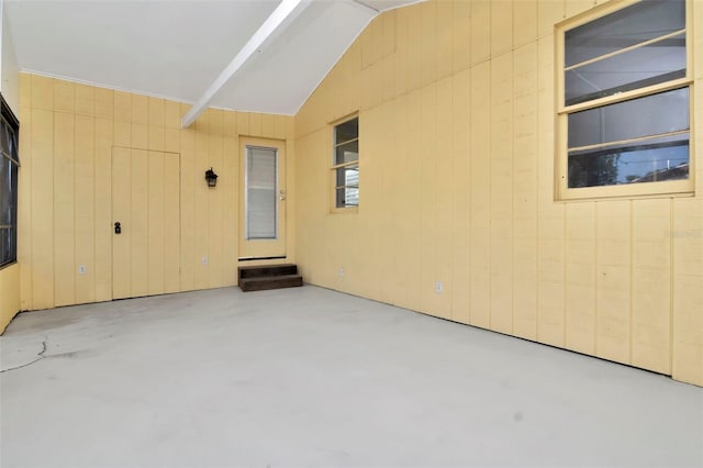 unfurnished room featuring finished concrete floors, vaulted ceiling, and wooden walls