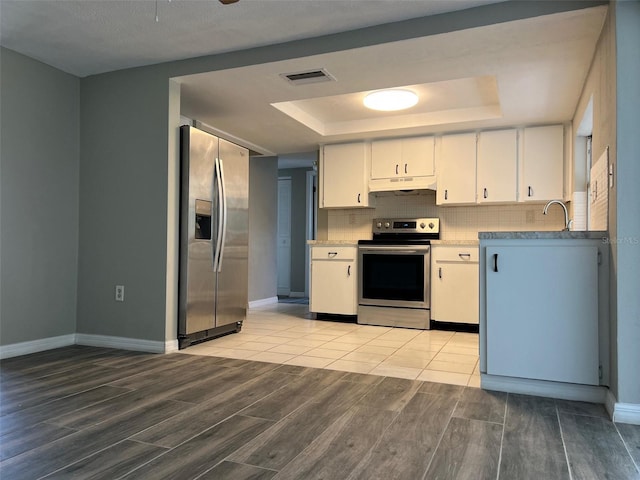 kitchen featuring appliances with stainless steel finishes, a tray ceiling, under cabinet range hood, wood finish floors, and white cabinets