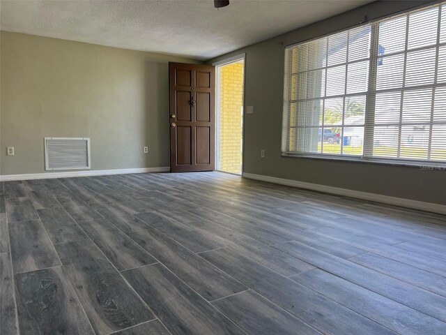 unfurnished living room featuring dark wood-style flooring, a textured ceiling, and baseboards