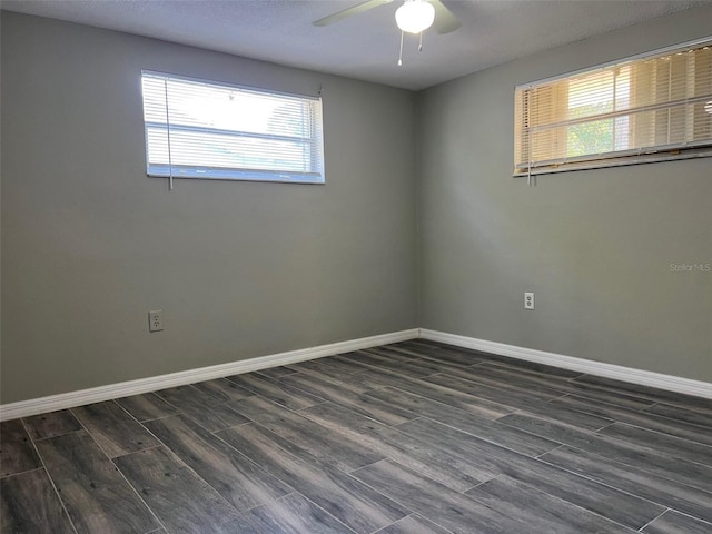 spare room featuring healthy amount of natural light, a ceiling fan, dark wood-style flooring, and baseboards