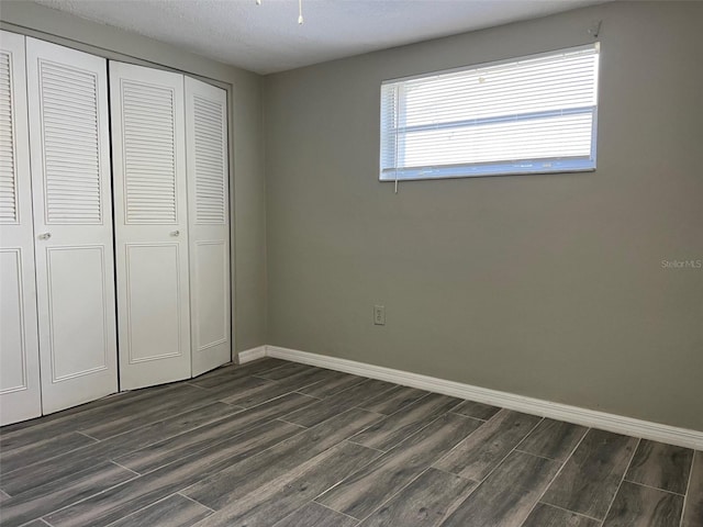 unfurnished bedroom with dark wood finished floors, baseboards, and a closet