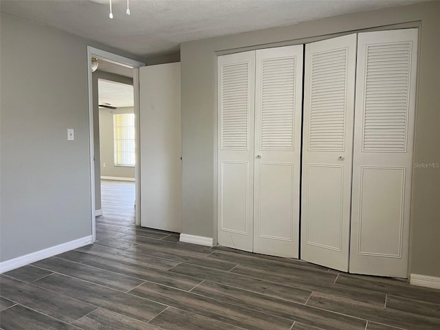 unfurnished bedroom featuring baseboards, a closet, dark wood-style flooring, and a textured ceiling