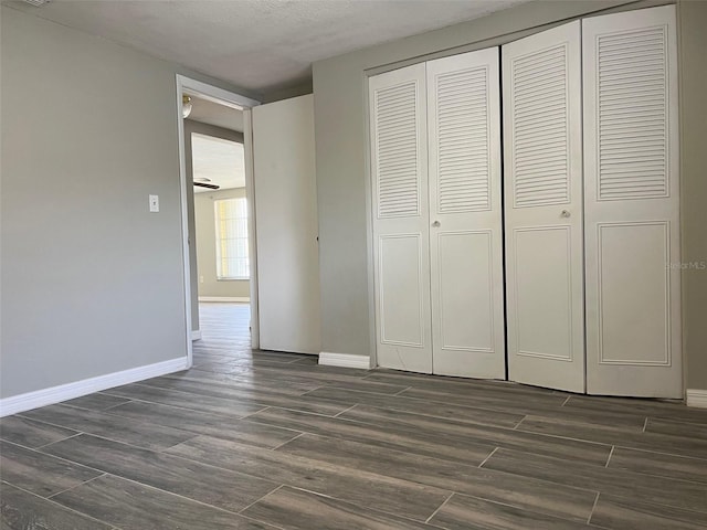 unfurnished bedroom featuring a closet, baseboards, dark wood-type flooring, and a textured ceiling