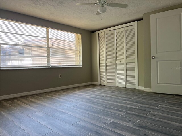 unfurnished bedroom featuring a textured ceiling, dark wood-style flooring, a closet, baseboards, and ceiling fan
