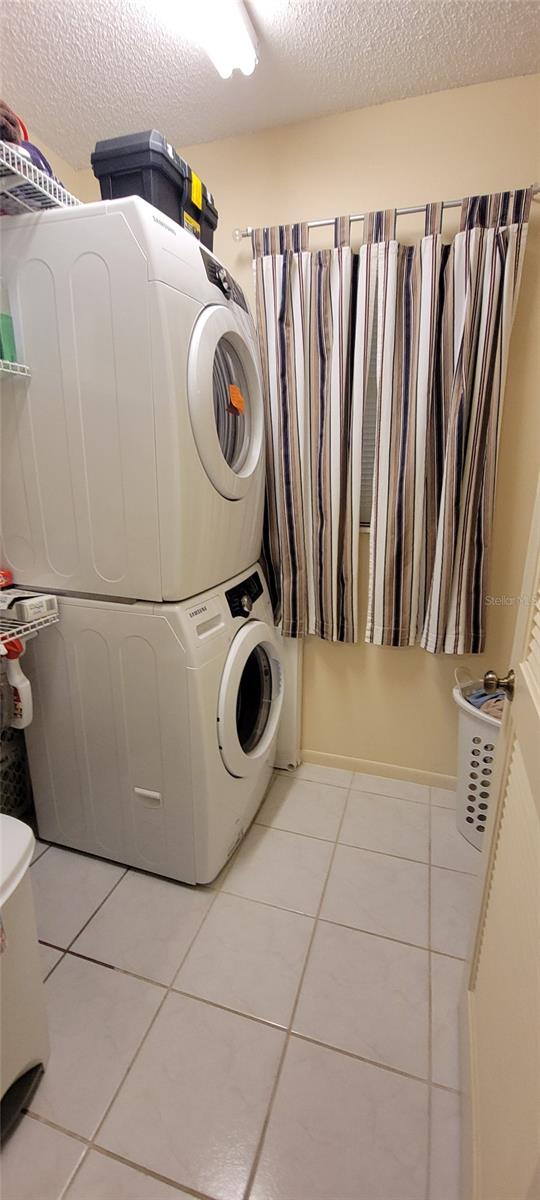 laundry area with estacked washer and dryer, a textured ceiling, and light tile patterned floors