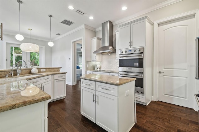 kitchen with wall chimney exhaust hood, a sink, double oven, ornamental molding, and a center island