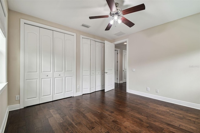 unfurnished bedroom with two closets, baseboards, dark wood-type flooring, and ceiling fan