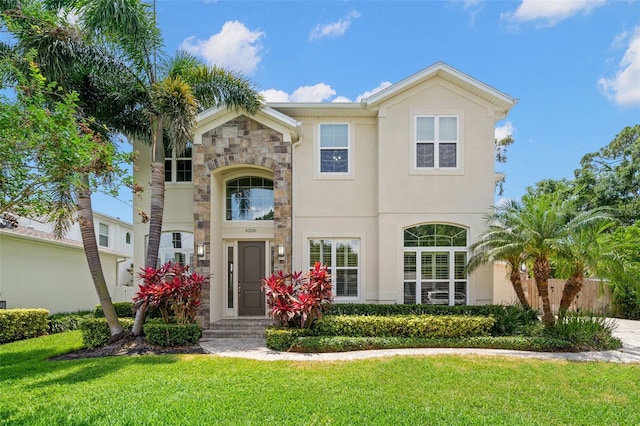 view of front of property with a front yard, stone siding, and stucco siding