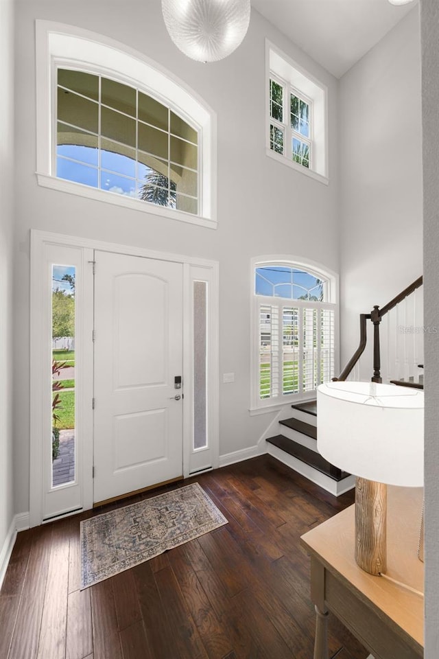 foyer with a towering ceiling, baseboards, dark wood-type flooring, and healthy amount of natural light