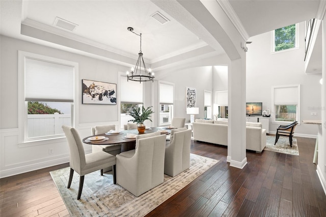 dining space featuring a tray ceiling, dark wood-style flooring, a chandelier, crown molding, and wainscoting