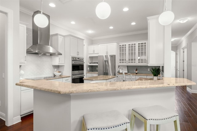 kitchen featuring appliances with stainless steel finishes, wall chimney range hood, a sink, light stone countertops, and tasteful backsplash