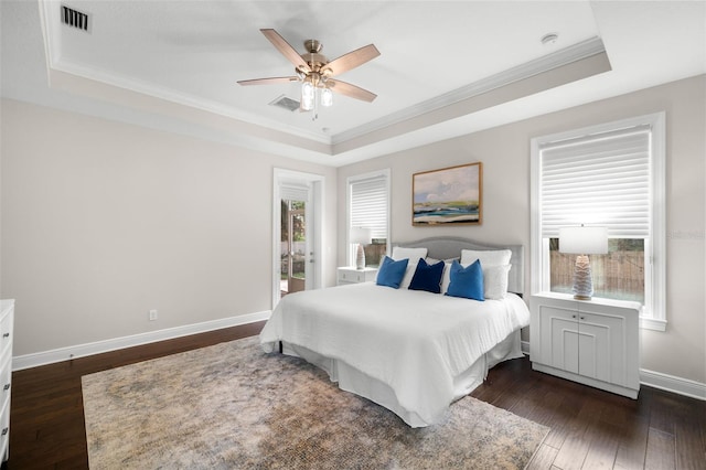 bedroom with a raised ceiling, ornamental molding, dark wood-style floors, baseboards, and a ceiling fan