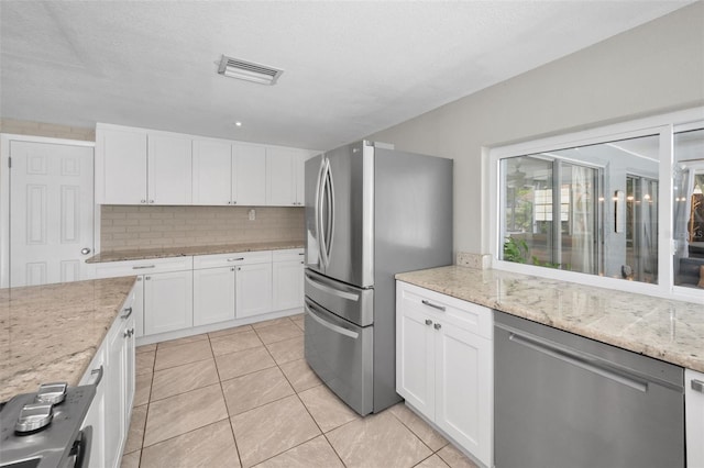 kitchen featuring appliances with stainless steel finishes, tasteful backsplash, white cabinets, light tile patterned flooring, and light stone countertops