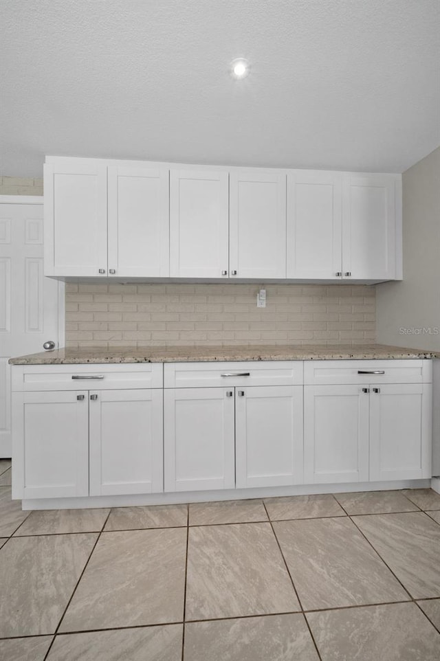 kitchen with light stone countertops, white cabinetry, tasteful backsplash, light tile patterned flooring, and a textured ceiling