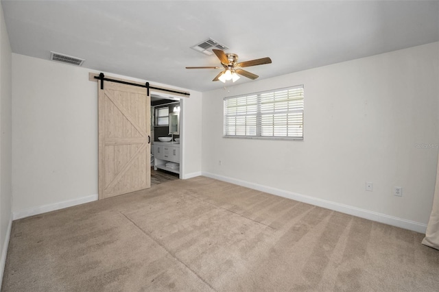 unfurnished bedroom featuring a barn door, carpet flooring, baseboards, ensuite bath, and ceiling fan