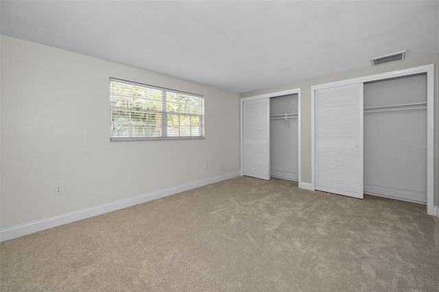 unfurnished bedroom featuring multiple closets, carpet flooring, and baseboards